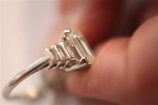 A 1930s/1940s Art Deco platinum and single stone emerald cut diamond ring, with graduated baguette cut diamond set shoulders,